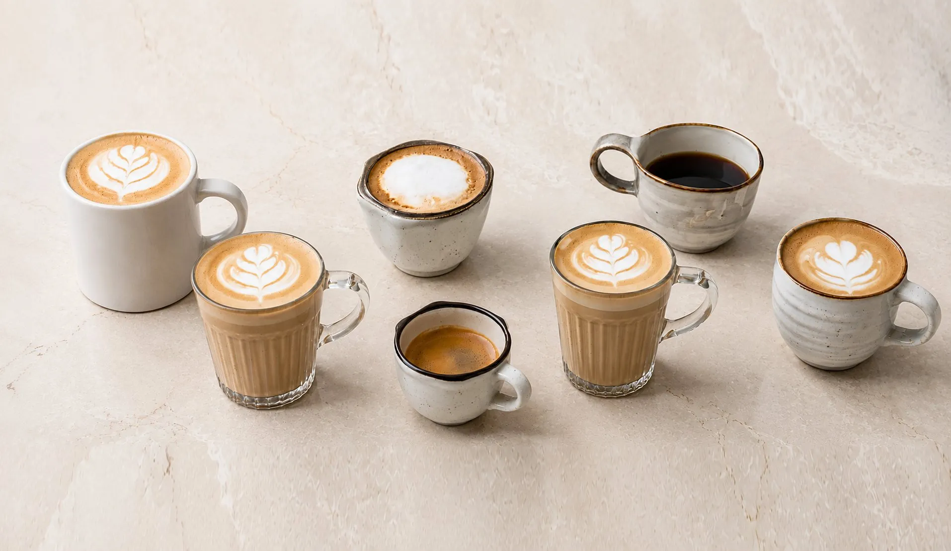 Tazas de café de especialidad sobre una mesa de mármol: varias con arte en leche, un espresso corto y un americano