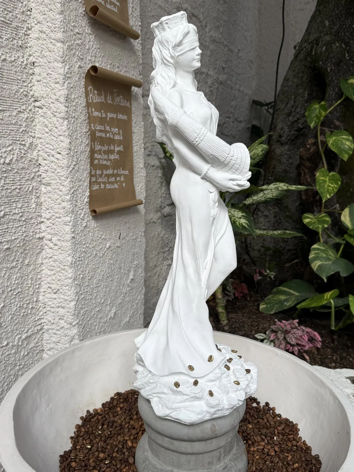 Fuente de CAELUS con una figura de Fortuna en piedra blanca, rodeada de granos de café dorados