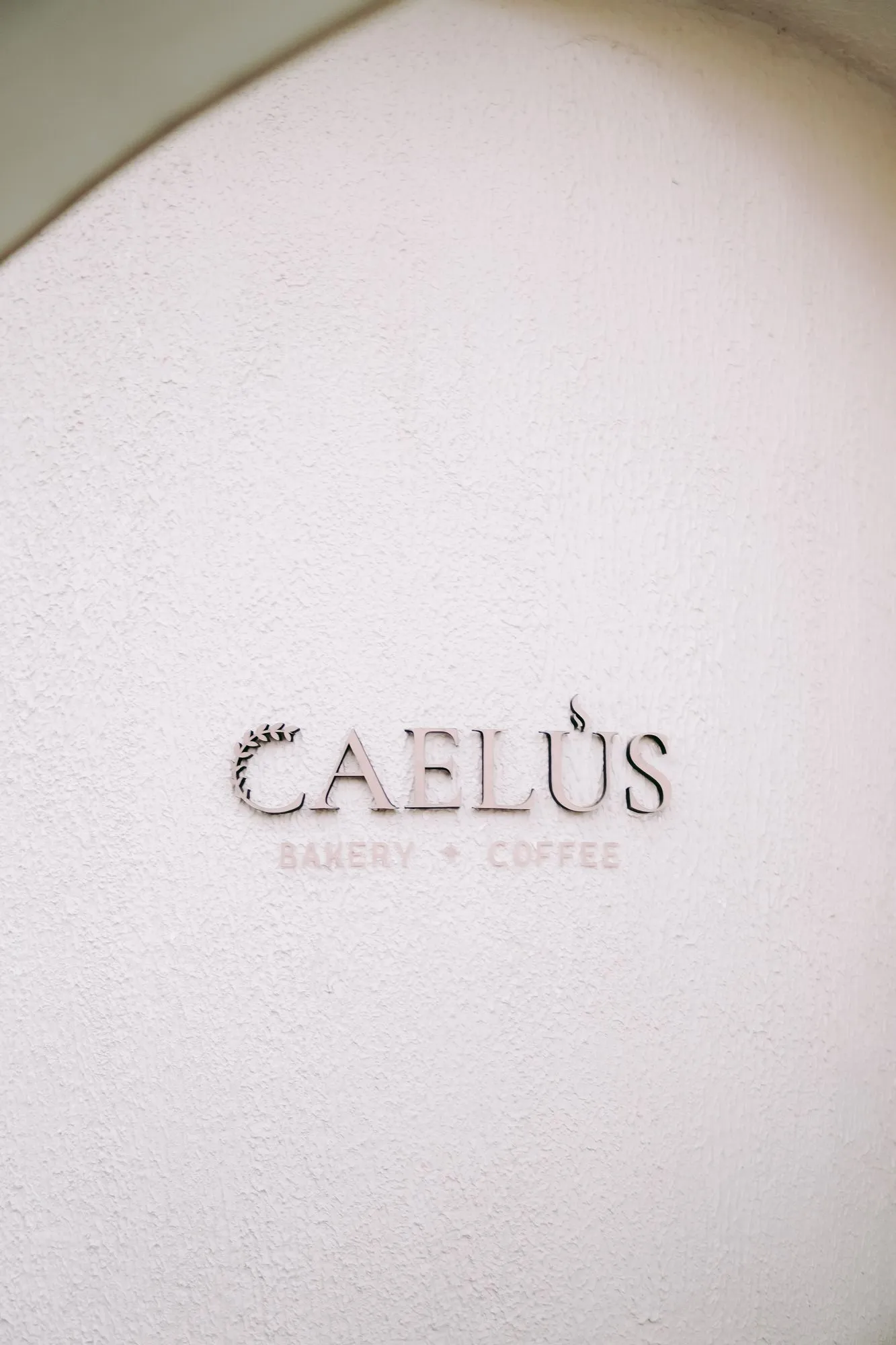 Logo de CAELUS Bakery Coffee grabado en relieve sobre el muro del local
