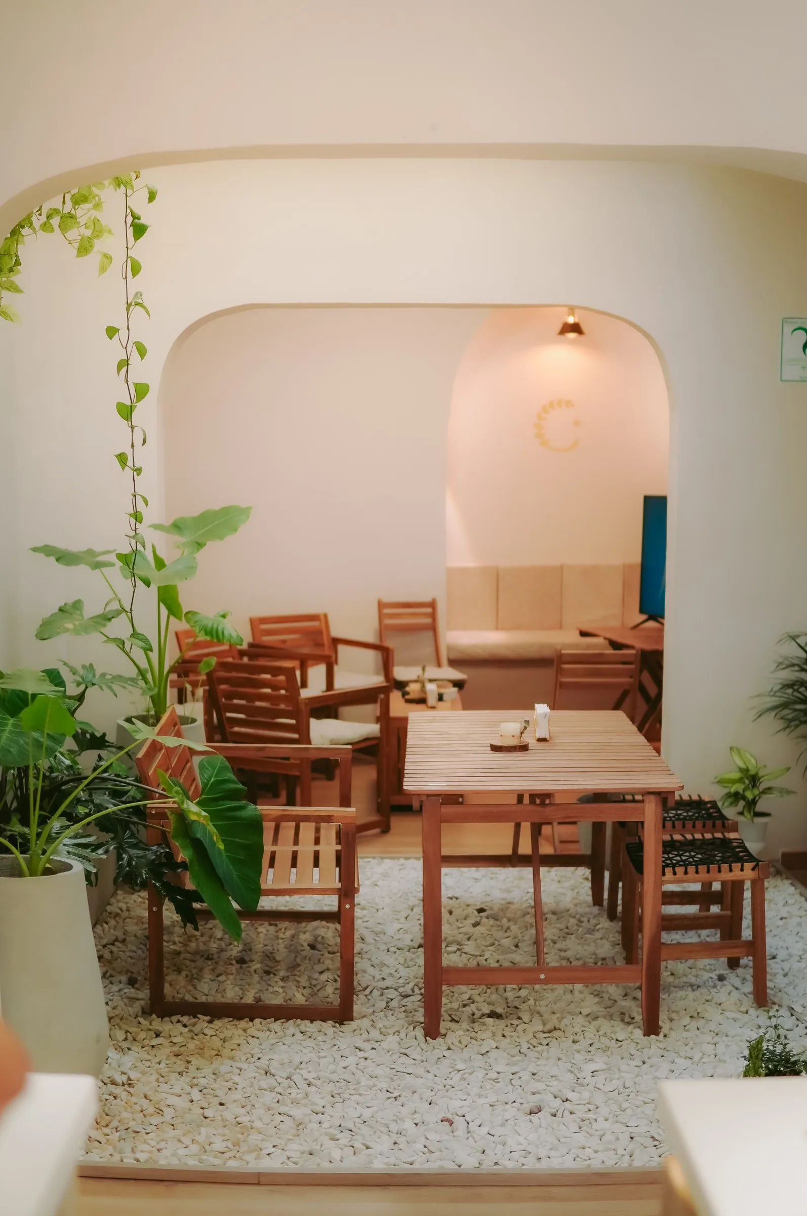 Patio interior de CAELUS visto a través de un arco de obra, con plantas, gravilla blanca y mesas de madera