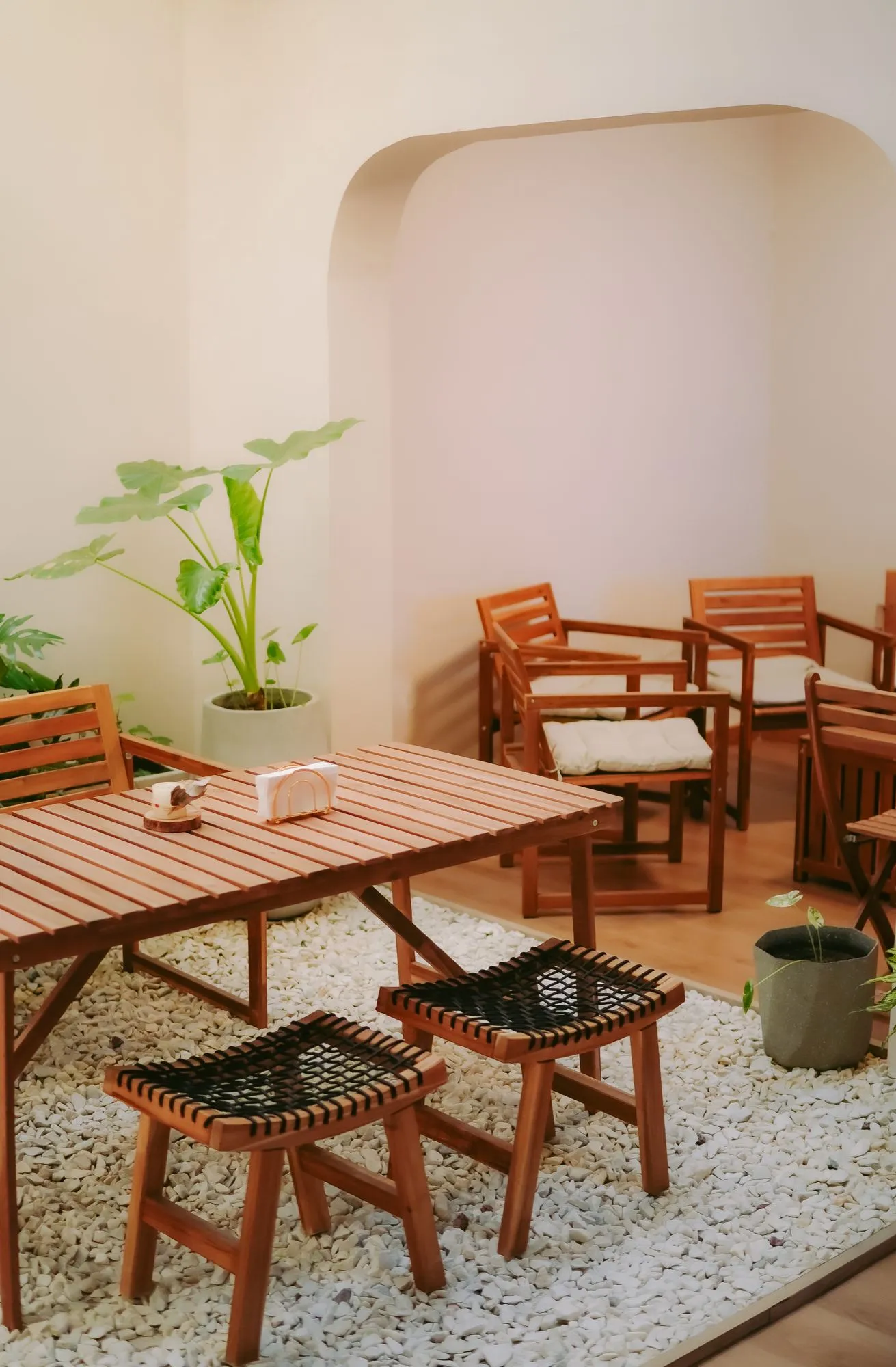 Mesa de madera con banquetas sobre gravilla blanca, junto a un arco, en el patio interno de CAELUS